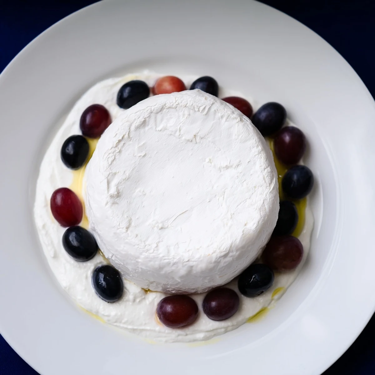 Floating Island recipe: A creamy cheese wheel floating on vibrant blue yogurt amidst dark grapes.
