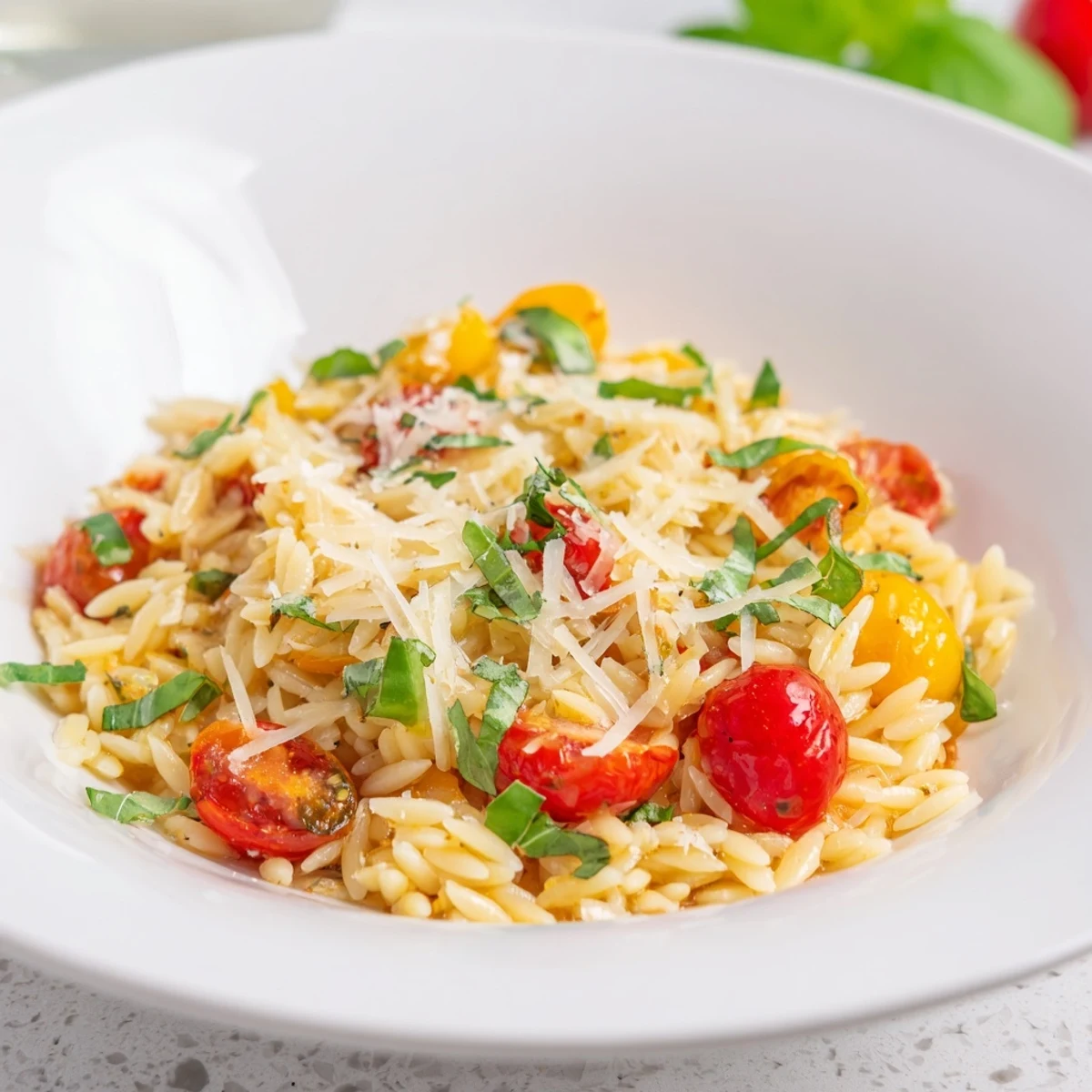Vibrant bowl of cooked Orzo Tomato Parmesan with glistening olive oil and fresh basil garnish.