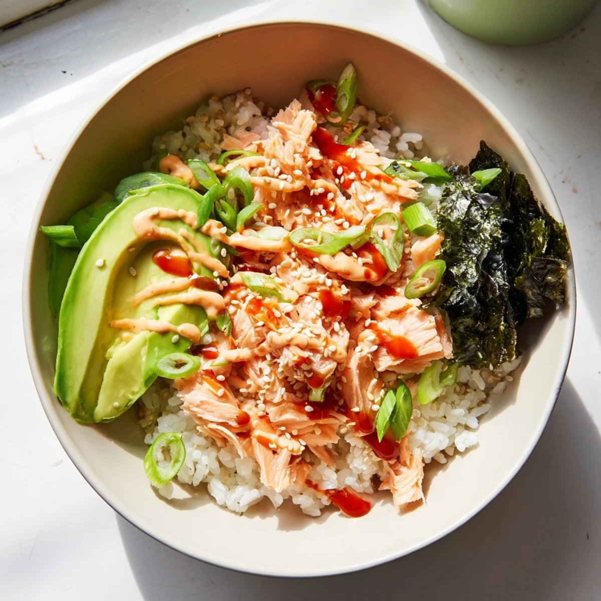 A generous serving of Emily Mariko Salmon Rice Bowl garnished with sesame seeds and green onions, served with crispy nori sheets.