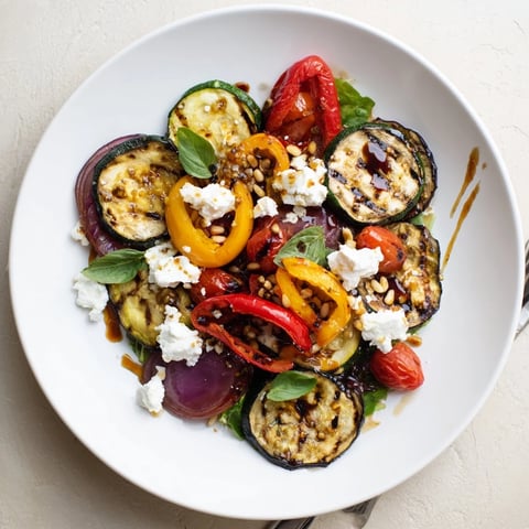 A colorful grilled vegetable and goat cheese salad with fresh greens and vinaigrette.  