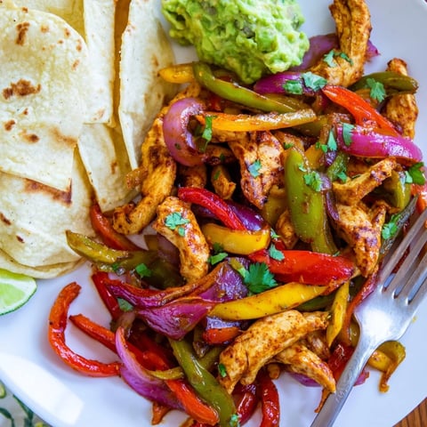 Colorful sheet pan chicken fajitas garnished with fresh cilantro and lime wedges.  