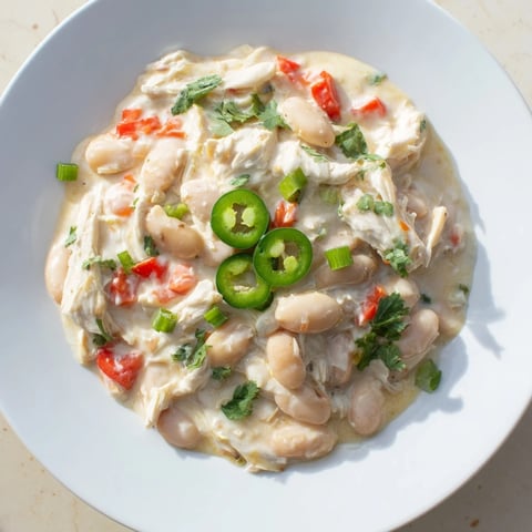 A steaming bowl of Creamy White Chicken Chili with beans, garnished with fresh cilantro and cheese.