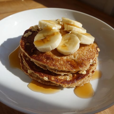 Golden-brown Banana Oat Pancakes stacked, drizzled with syrup, a perfect, comforting breakfast plate.