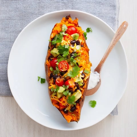 Steaming Loaded Baked Sweet Potatoes, filled with black beans, tomatoes, and creamy avocado, ready to eat.
