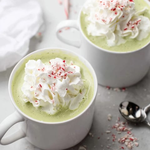 A vibrant Cozy Peppermint Matcha Christmas Latte, rich green color topped with whipped cream and crushed candy.