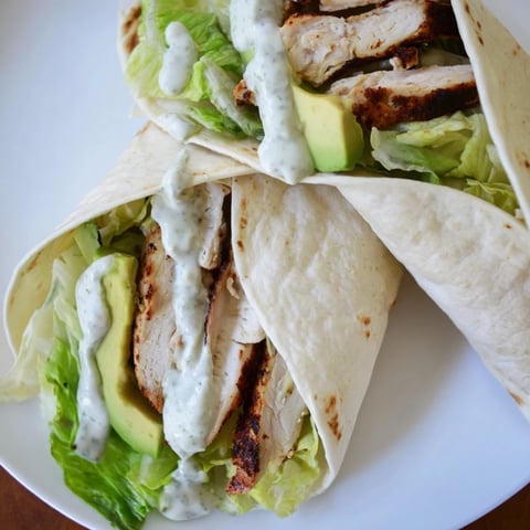 A close-up of Smoky Chipotle Chicken Wrap filled with sliced grilled chicken, creamy avocado, and crisp lettuce, drizzled with tangy Greek yogurt sauce.  