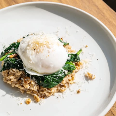 Steaming Savoury Oatmeal with Spinach & Poached Egg topped with runny egg yolk and fresh pepper flakes.