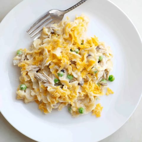 A close-up shot of a steaming, cheesy Creamy Tuna Noodle Casserole with fresh peas.
