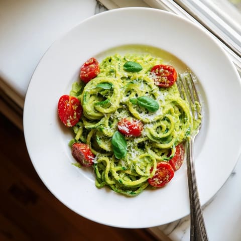 Green zoodles tossed in creamy avocado pesto, garnished with cherry tomatoes for a light and healthy Italian-inspired meal.