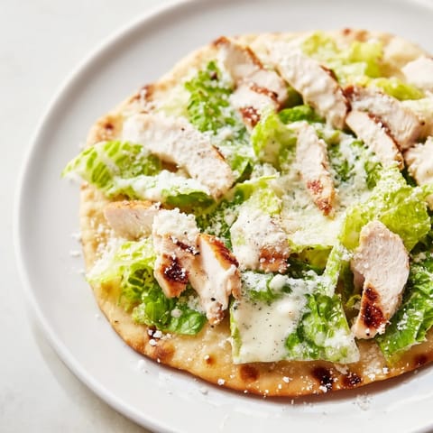 The warm flatbread is drizzled with creamy Caesar dressing and halved cherry tomatoes, creating a vibrant and appetizing lunch option.