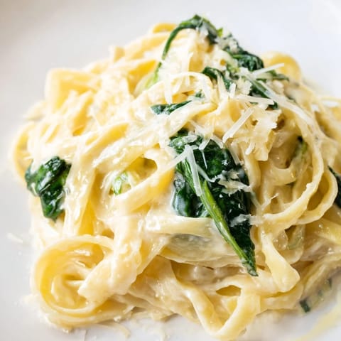 Creamy garlic spinach pasta twirls on a fork beside fresh parsley garnish.