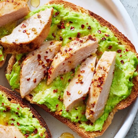 Serving of Smashed Avocado Chicken Toast, featuring juicy sliced chicken on avocado-covered toast, with a sprinkle of chili flakes and fresh cilantro garnish.