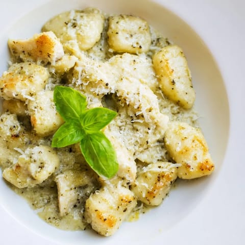 A close-up of Creamy Pesto Gnocchi with Chicken on a white plate, highlighting rich green pesto sauce and tender chicken bites.  