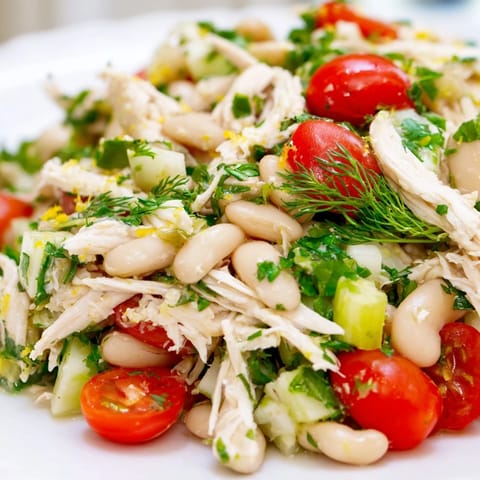 A vibrant bowl of Lemony White Bean Chicken Salad, garnished with cherry tomatoes and parsley, served on a rustic wooden table.  