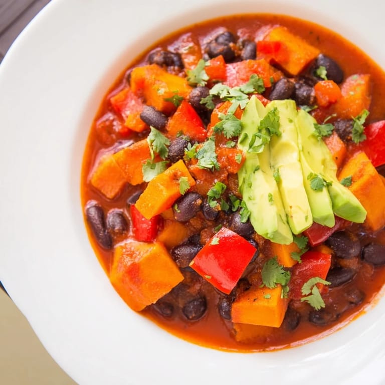 A visually appealing bowl of hearty Sweet Potato & Black Bean Chili, garnished with lime wedges for serving.