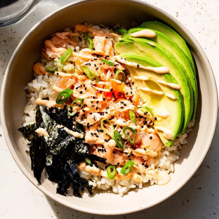 Top-down view of a bubbling Emily Mariko Salmon Rice Bowl in a microwave-safe bowl, ready to be topped with fresh avocado.
