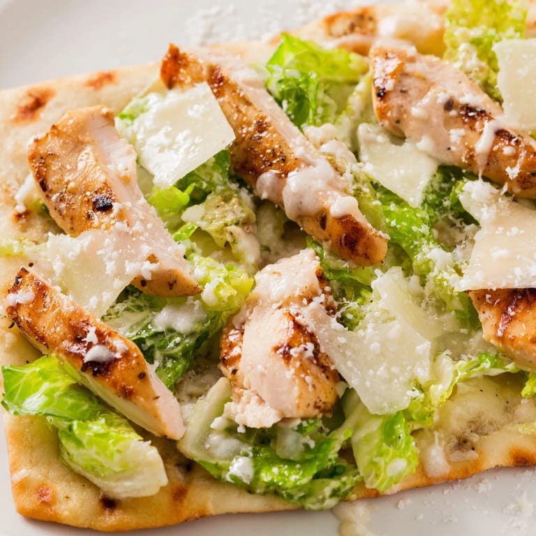 Sliced pieces of Chicken Caesar Flatbread reveal juicy grilled chicken and crisp romaine on a wooden serving board.
