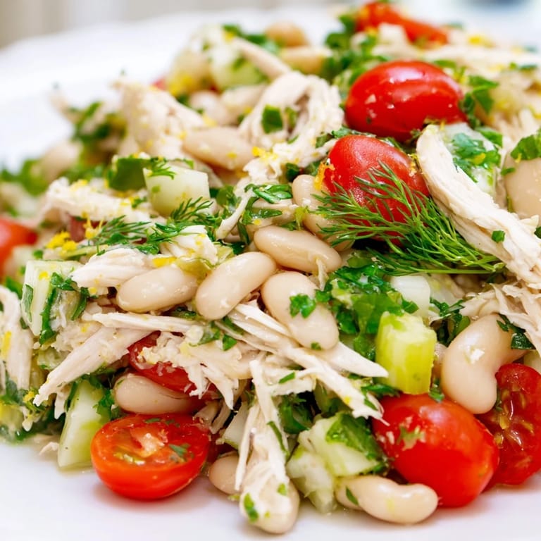 A vibrant bowl of Lemony White Bean Chicken Salad, garnished with cherry tomatoes and parsley, served on a rustic wooden table.  