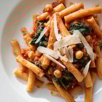 Creamy Tuscan Chickpea Pasta served in a rustic bowl, garnished with fresh basil and Parmesan alongside a glass of white wine.